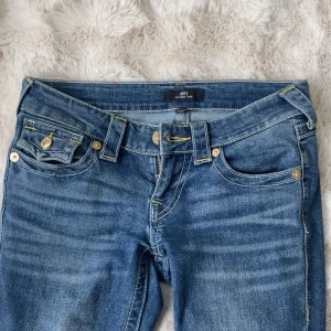 Blå bootcut jeans från True Religion - Säljer ett par klassiska blå jeans från True Religion med bootcut passform. De är lågmidjade och storlek 23 ja e 160 och de är ganska långa.