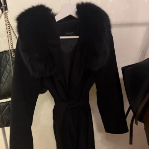 Svart kappa Hollies  - Äkta päls strl 32 men är en 34/36!! Bandet sitter inte fast med hakar i jackan, men det kan man enkelt lösa själv om man vill ha det. Nypris 7.000:-