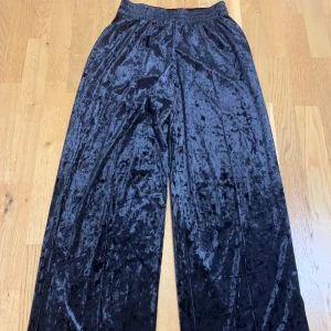 Svarta sammetsbyxor från Gina Tricot - Säljer ett par svarta sammetsbyxor från Gina Tricot med resår i midjan. Byxorna har en loose passform och är tillverkade i mjuk, glansig sammet som ger en lyxig känsla. Perfekta för dig som vill ha både stil och komfort.