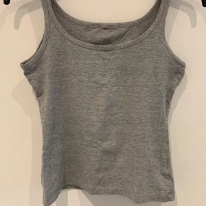 Grått baslinne - Säljer ett enkelt grått linne med rund halsringning och smala axelband. Perfekt att ha som basplagg till olika outfits. Gjort i mjuk bomull för en bekväm känsla.