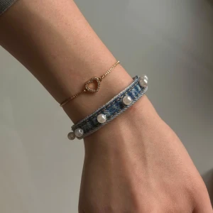 Denim armband - Unikt armband i ljusblått återvunnet jeansmaterial som även är handgjort och dekorerat med vita pärlor och guldfärgade metalldetaljer i rostfritt stål. Armbandet har en justerbar kedja för perfekt passform och själva jeansdelen är 12 cm lång. Kolla gärna in vår instagram: Jeanfluence.uf