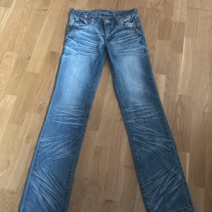 Blåa lågmidjade jeans  - Säljer dessa lågmidjade jeans med snygga detaljer. Innerbenmåttet är 82 cm och midjemåttet är 38 cm takt över. Skriv ifall fler bilder önskas🤍