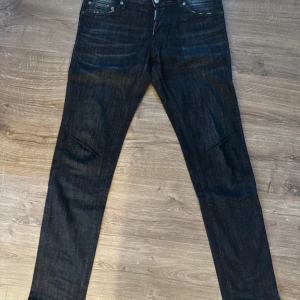 Svarta jeans från Dsquared2 - Säljer ett par svarta jeans från Dsquared2 med klassisk femficksdesign och diskreta slitningar. Jeansen har normal passform och raka ben. Tillverkade i Italien och i ett robust denimtyg. Perfekta för dig som gillar stilrena och exklusiva jeans. Storlek ( 48) sitter som w32