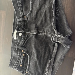 Svarta jeansshorts med råa kanter - Svarta jeansshorts med fransiga, råa kanter och klassisk femficksdesign. Gylf med dragkedja och knapp framtill. Perfekta för en avslappnad stil. Jätte fina till sommaren har packat dom redan då en tjej ville ha dom men ångrade sig så skickar direkt när någon köpt ❤️