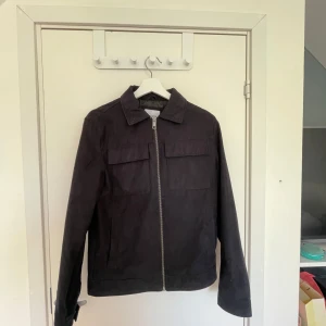 Svart jacka från Jack & Jones med dragkedja - Säljer en svart jacka från Jack & Jones med klassisk krage och två bröstfickor. Jackan har rak passform och stängs med en grov dragkedja framtill. Perfekt för dig som gillar en stilren och enkel look.