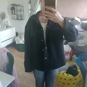 Svart kappa med fickor  - Svart kappa med silvriga knappar. Kappan har två bröstfickor och är långärmad. Står ingen storlek men jag skulle säga att den är i S. 