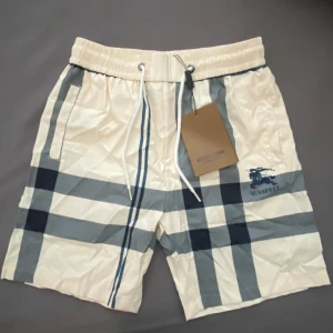 Burberry shorts - Snygga shorts med klassiskt rutigt mönster i grått och blått från Burberry. De har resårmidja med vit snörning och två sidofickor. Perfekta för sommardagar och har en modern, avslappnad look. Heltnya