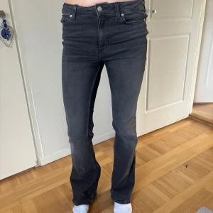 Grå bootcut jeans - Snygga grå jeans med bootcut passform och klassiska fem fickor. Jeansen har mid/ hög midja och raka ben som blir vidare nedtill. Perfekta för en stilren och avslappnad look.