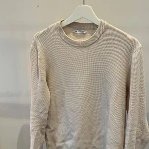 Beige stickad tröja från Zara - Säljer en stilren beige stickad tröja från Zara. Tröjan har rund halsringning och långa ärmar, perfekt för lager-på-lager eller som den är. Enkel och tidlös design som passar till det mesta.
