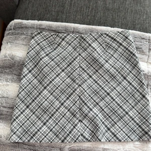 Grå och vit rutig kjol - Säljer en snygg grå och vit rutig kjol med klassiskt mönster. Kjolen har en rak passform och är kort i modellen, perfekt till vardags eller när du vill känna dig extra stylish. Passar dig som gillar en tidlös look.