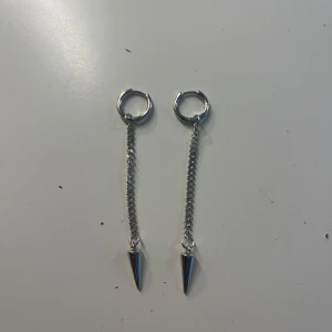 Silverfärgade örhängen med kedja och konformad detalj - Säljer ett par coola silverfärgade örhängen med tunn kedja och spetsig konformad detalj längst ner. Perfekta för dig som gillar en edgy och modern stil. Passar till många olika looks! Självklart rengjorda tror bara använd 1 gång. I äkta silver!