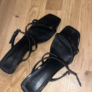 Klackar - Säljer ett par svarta sandaler med smala remmar och fyrkantig tå. Skorna har en låg klack och är i glansigt syntetmaterial. De är från H&M och har använts ett fåtal gånger 🫶 kontakta för mer information och pris 