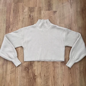 Snygg beige ribbad croppad polotröja från Gina Tricot - Säljer en beige ribbad croppad polotröja från Gina Tricot. Tröjan har långa ärmar med breda muddar och hög krage. Materialet är en mix av viskos, polyester och polyamid vilket gör den mjuk och stretchig. Perfekt till lager-på-lager-stil.