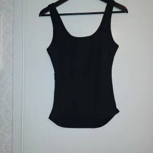 Svart linnetopp - En stilren svart linnetopp med breda axelband och rundad halsringning. Perfekt att matcha med jeans eller kjol för en enkel och snygg look.Endast tvättad
