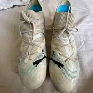 Puma fotbollsskor med snörning - Säljer ett par fotbollsskor från Puma med svart logga på ovansidan. Skorna har snörning, stickad strumpliknande öppning och rosa dobbar undertill. Perfekta för dig som vill ha snygga och bekväma skor på planen.