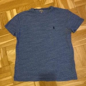 Blå t-shirt från Ralph Lauren - Säljer en snygg blå t-shirt från Ralph Lauren i storlek S med det klassiska broderade logotypen på bröstet. T-shirten är kortärmad och gjord i mjukt material, perfekt för en avslappnad stil. 