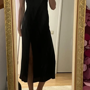 Svart klänning från H&M - Säljer en elegant svart klänning från H&M med korta puffärmar och en smickrande passform. Klänningen har en slits som ger en extra touch av stil. Perfekt för en kväll ute eller en speciell tillställning.