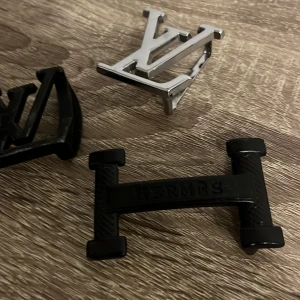 Bältespännen  - Säljer tre bältespännen i metall med olika design. Ett i silverfärg och två i svart, alla med distinkta logotyper. Perfekt för att ge din outfit en unik touch. Väldigt fina samt användbara för dig som gillar Hrm, Lv mm.! Mvh ItsForFits 🌟