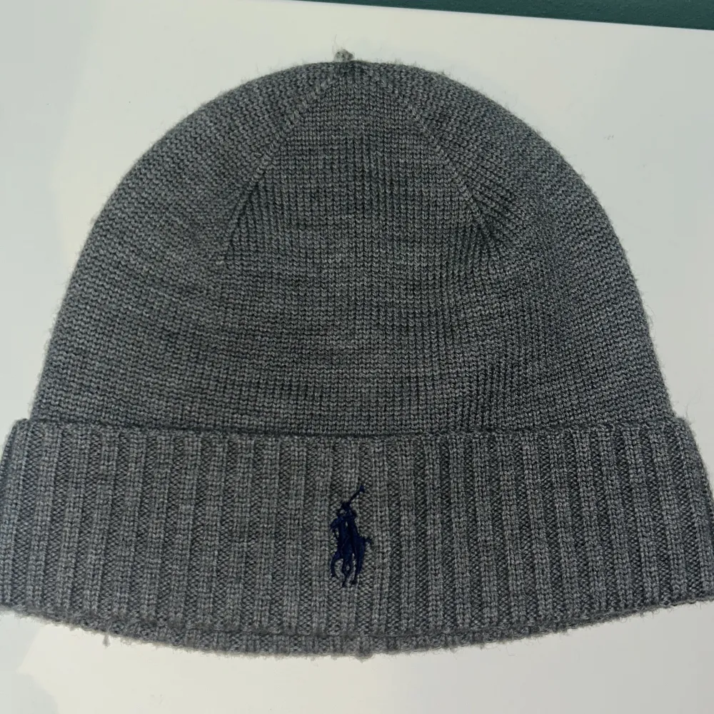 Snygg grå stickad mössa från Ralph Lauren med broderad logga framtill. Perfekt för kyliga dagar och ger en stilren look. Passar både till vardags och mer uppklädda tillfällen.. Asusteet.