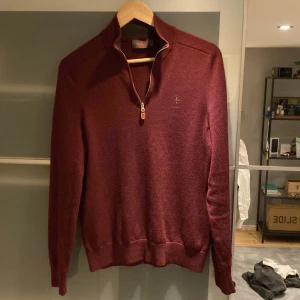 Vinröd tröja med dragkedja - Säljer en stilren vinröd tröja från Gant med dragkedja vid halsen. Tröjan har långa ärmar och en liten broderad logga på bröstet. Perfekt för kyligare dagar.