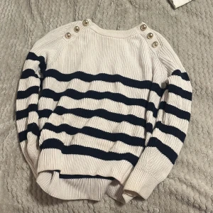 Randig stickad tröja med knappar - Säljer en mysig  tröja med marinblå och vita ränder. Tröjan har dekorativa knappar på axlarna och långa ärmar. 100% Bomull. Lite använd. Storlek S. Hör av dig för eventuella frågor 🌸kolla gärna in mina andra annonser!⤵️✨