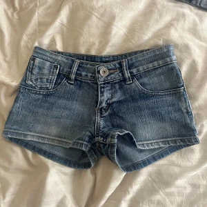 Blå jeansshorts  - Snygga blå jeansshorts med klassisk femficksdesign och knappgylf. Perfekta för varma sommardagar. De har en lätt tvättad look och är lågmidjade för en avslappnad stil.