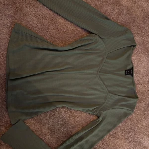 Grön ribbad topp  - Snygg grön ribbad topp med långärmad design. Perfekt för en stilren look. Toppen har en figurnära passform och är tillverkad i ett mjukt material.