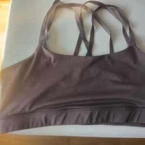 Brun sporttopp från H&M Move - Säljer en brun sporttopp från H&M Move med dubbla axelband som korsas i ryggen. Perfekt för träning med sin bekväma passform och stilrena design. Toppen är tillverkad i ett mjukt och stretchigt material.