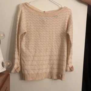 Rosa stickad tröja med knyt - Säljer en söt beige stickad tröja med ett diskret mönster och knyt i ryggen. Tröjan har långa ärmar och ribbade kanter. Perfekt för en mysig dag.