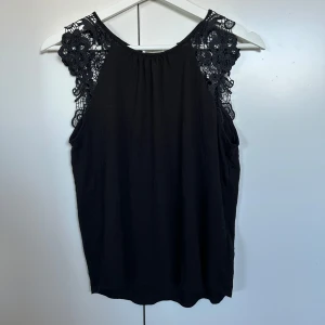 Svart topp med spetsdetaljer - Snygg svart ärmlös topp med vackra spetsdetaljer på axlarna. Jätte fin och aldrig använd.❤️
