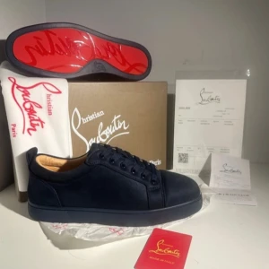Svarta sneakers från Christian Louboutin - Snygga svarta sneakers från Christian Louboutin med den ikoniska röda sulan. Skorna har en stilren design med snörning och är tillverkade i skinn. Perfekta för den som vill ha en lyxig touch i vardagen.