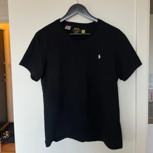 Svart t-shirt från Polo Ralph Lauren - Säljer en klassisk svart t-shirt från Polo Ralph Lauren med en liten broderad logga på bröstet. T-shirten är kortärmad och tillverkad i mjuk bomull. Perfekt för en stilren look. Nypris 999kr