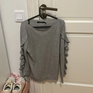 Grå tröja från Ralph Lauren - Säljer en stilren grå tröja från Ralph Lauren med volangdetaljer längs ärmarna. Perfekt för en elegant look. Tröjan har en normal passform och är tillverkad i ett mjukt material. Använd fåtal gånger, pris går att diskutera🩷🩷