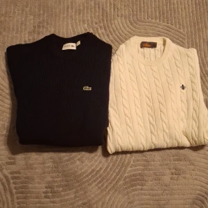 2 snygga tröjor - Två snygga stickade tröjor, en svart från Lacoste med deras ikoniska logga och en vit från Gant med ett diskret emblem. Perfekta för kyligare dagar och ger en stilren look.