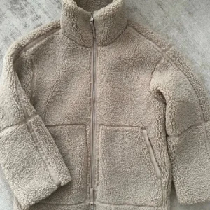 Teddyjacka hm - Mysig beige teddyjacka med dragkedja framtill och hög krage. Jackan har långa ärmar och två praktiska fickor. Perfekt för kyliga dagar när du vill hålla dig varm och bekväm.