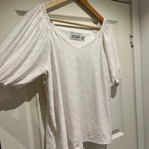 Vit blus från ICHI - Säljer en söt vit blus från ICHI med v-ringning och puffiga kortärmar. Blusen har ett diskret broderat mönster. Storlek XS men är stor i storleken