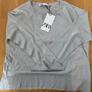 Silverfärgad tröja från Zara - Snygg silverfärgad tröja från Zara med en glittrig finish. Tröjan har långa ärmar och en rund halsringning, perfekt för att lägga till lite glamour i vardagen. Den är tillverkad i ett mjukt och bekvämt material.