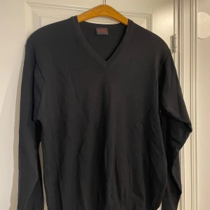 Svart tröja från Oscar Jacobson - Säljer en stilren svart tröja från Oscar Jacobson med v-ringning. Tröjan har långa ärmar och är perfekt för en klassisk look. Passar bra till både jeans och chinos. Perfekt för höst och vinter!