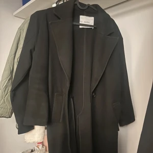 Svart kappa från Bershka - Snygg svart kappa från Bershka med klassisk design. Den har långa ärmar och en stilren look som passar perfekt för kyligare dagar. Perfekt för att hålla stilen i höst och vinter.