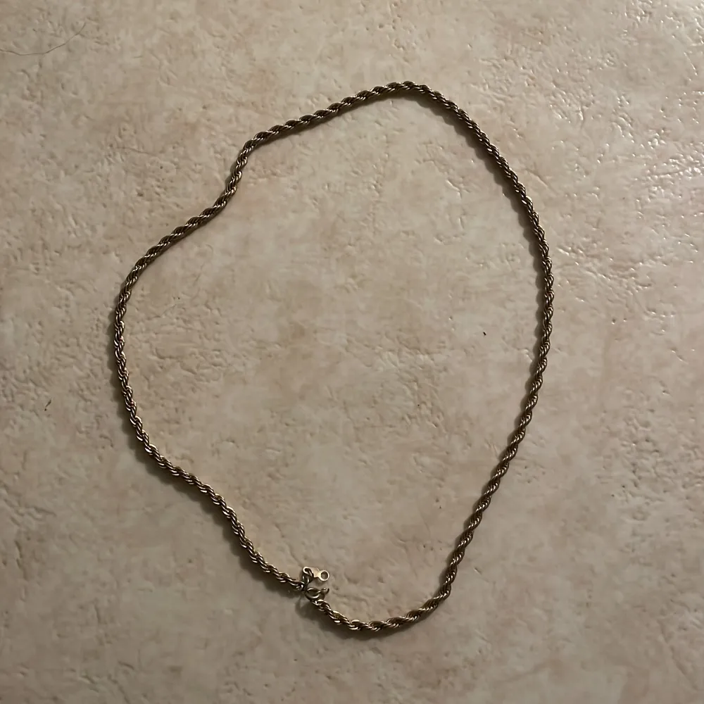 Snyggt guldfärgat halsband med en elegant tvinnad design. Perfekt för att ge en stilren touch till din outfit. Halsbandet har en klassisk låsning som gör det enkelt att ta på och av.. Asusteet.