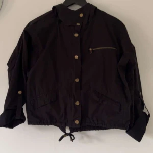 Svart jacka från Vero Moda - Säljer en svart jacka från Vero Moda i storlek XS. Jackan har en dragkedja och knappar framtill samt en praktisk huva. Perfekt för svala dagar med sin stilrena design och bekväma passform.