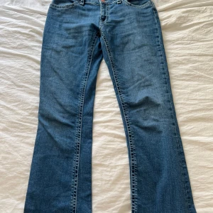 Blå jeans med bootcut - Snygga blå jeans med bootcut-stil och klassisk femficksdesign. De har en knapp och dragkedja framtill samt dekorativa sömmar på bakfickorna. Perfekta för en avslappnad look.