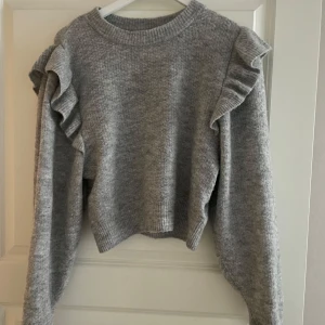 Grå stickad tröja från Divided - Säljer en mysig grå stickad tröja från H&M Divided med volangdetaljer på axlarna. Tröjan är perfekt för kyligare dagar. Den är både stilren och trendig, ett måste i garderoben! 💫