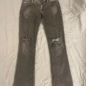 Grå bootcut jeans med slitningar - Snygga grå bootcut jeans med coola slitningar på framsidan och fransiga kanter. Perfekta för en avslappnad stil. De har en klassisk femficksdesign och en bekväm passform.