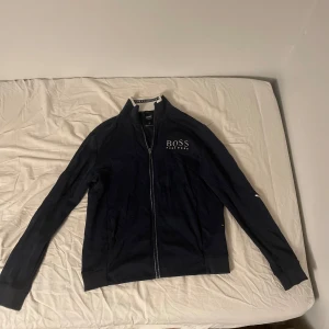 Mörkblå kofta från Hugo Boss - Säljer en stilren mörkblå kofta från Hugo Boss med dragkedja och märke på sidan av bröstet. Koftan har normal långa ärmar och en bekväm passform. Passar till nästan alla outfits. Fick den i present och de jag fick den av köpte den på  Pondus och den var för liten på mig då men orkade inte lämna tillbaka den så den har hängt i min garderob i ett tag. Priset går att diskutera vid en snabb o smidig affär😁