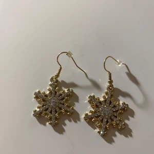 Guldiga snöflingeörhängen - Snygga guldiga örhängen i form av snöflingor, dekorerade med glittrande stenar. Perfekta för att ge en vinterkänsla till din outfit. De har en krok för enkel användning. Köpta på ur&penn💓