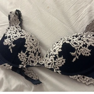 Mörkblå spets-bh - Elegant mörkblå bh med vacker vit spetsdetaljering. Den har breda axelband och en klassisk design som ger bra stöd och komfort. Perfekt för att känna sig både bekväm och stilfull. Orginal 519
