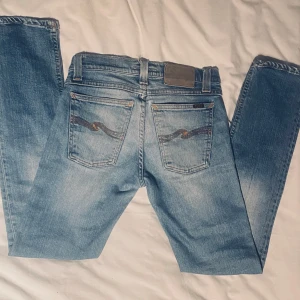 Ljusblå jeans från Nudie Jeans - Snygga ljusblå jeans från Nudie Jeans med klassisk femficksdesign och subtila slitningar. De har en knappgylf och är tillverkade i högkvalitativt denim. Perfekta för en avslappnad stil. W27 L30