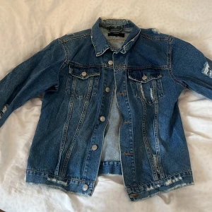 Blå oversized jeansjacka från Bik Bok - Säljer en snygg blå jeansjacka från Bik Bok i storlek XS. Jackan har en klassisk design med knappar framtill och slitna detaljer för en trendig look. Perfekt för att ge din outfit en cool touch.