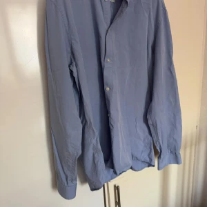 Bläck - Säljer en stilren blå skjorta från Bläck i storlek L. Skjortan har en klassisk design med knappar framtill och en regular fit. Perfekt för en snygg och avslappnad look.